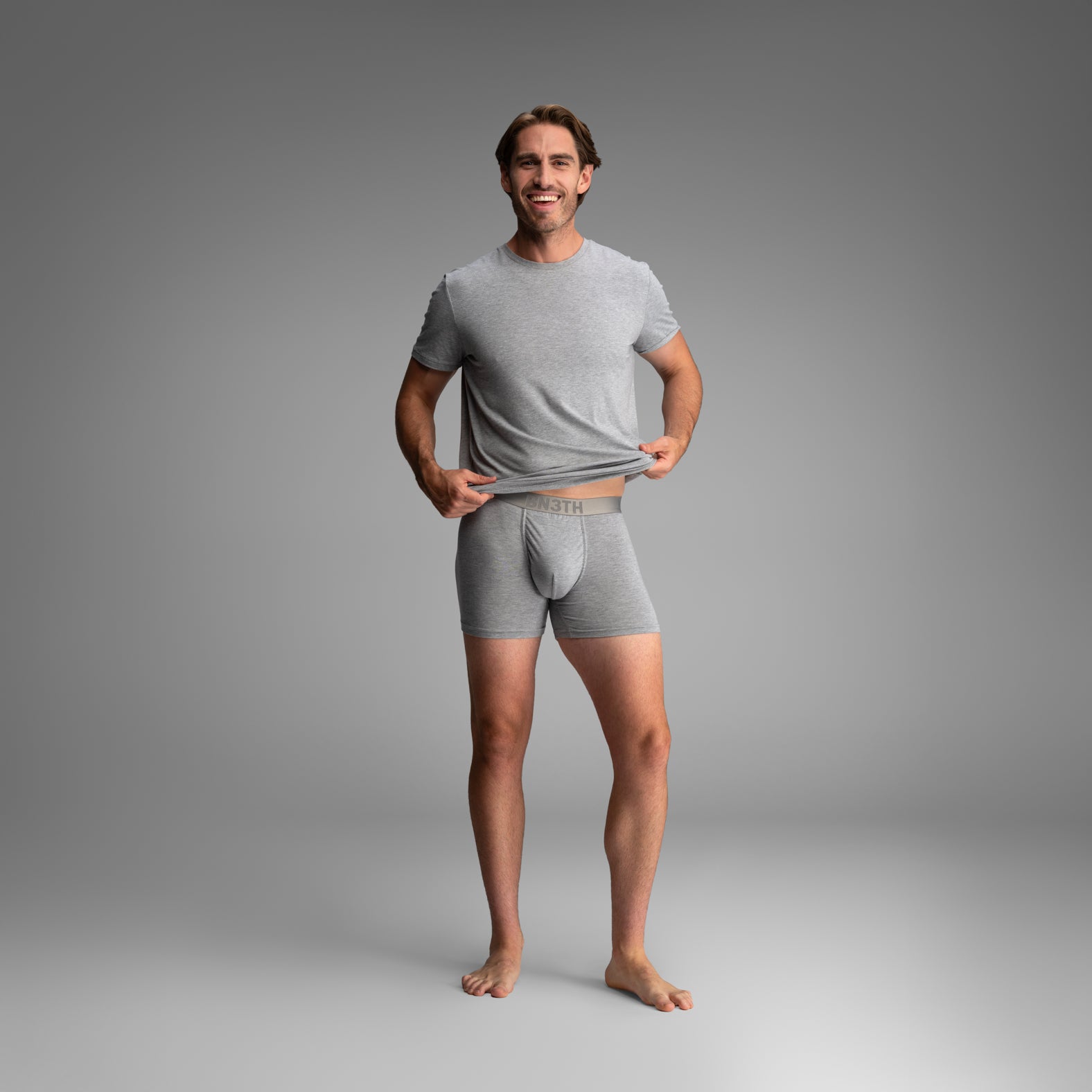 A man modeling a light gray heathered t-shirt and matching boxer briefs, standing against a neutral gray studio background. Essentials Boxer Brief: Heather Grey
